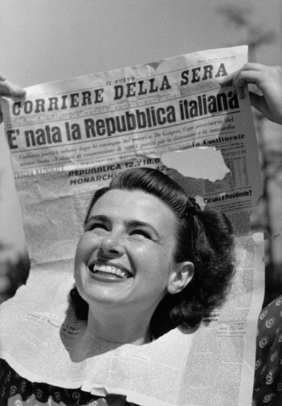 Photo en noir et blanc montrant le visage d'une jeune femme émergeant d'un exemplaire du Nuovo Corriere della Sera du 6 juin 1946 avec le titre 