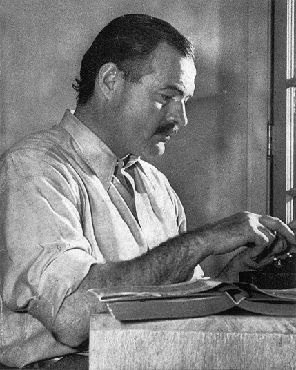 Illustration en noir et blanc d’Ernest Hemingway assis à une table, en train de taper sur une machine à écrire. Des documents sont visibles sur la table. L’arrière-plan montre une porte fermée et un mur.