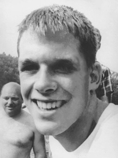 Photo rapprochée en noir et blanc du nageur américain Dick Roth, souriant et photographié en extérieur devant d'autres personnes.