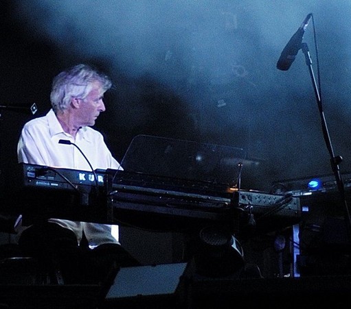 Photographie du musicien Richard Wright, assis devant un clavier électronique sur une scène éclairée. Il porte une chemise blanche et est concentré sur son instrument.