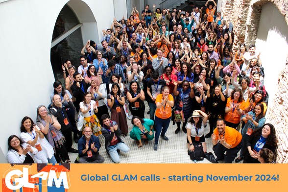 Group photo with more than 100 GLAM-Wiki practitioners from around the world, below a GLAM logo and banner advertising the GLAM-Wiki calls