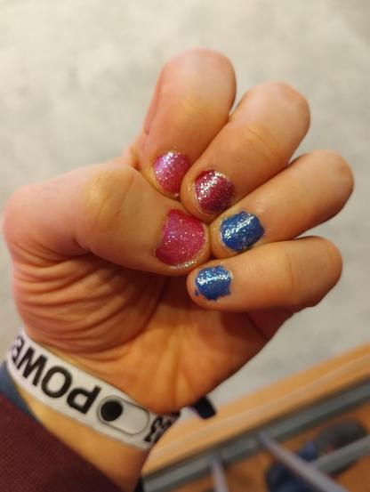 my left hand, with bi pride nails (glittery) and a 39c3 wristband