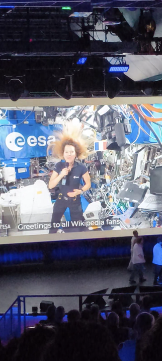 Sophie Adenot as seen on the screen of the Wikimania 2026 amphitheatre delivering a recorded message from the ISS to the audience.