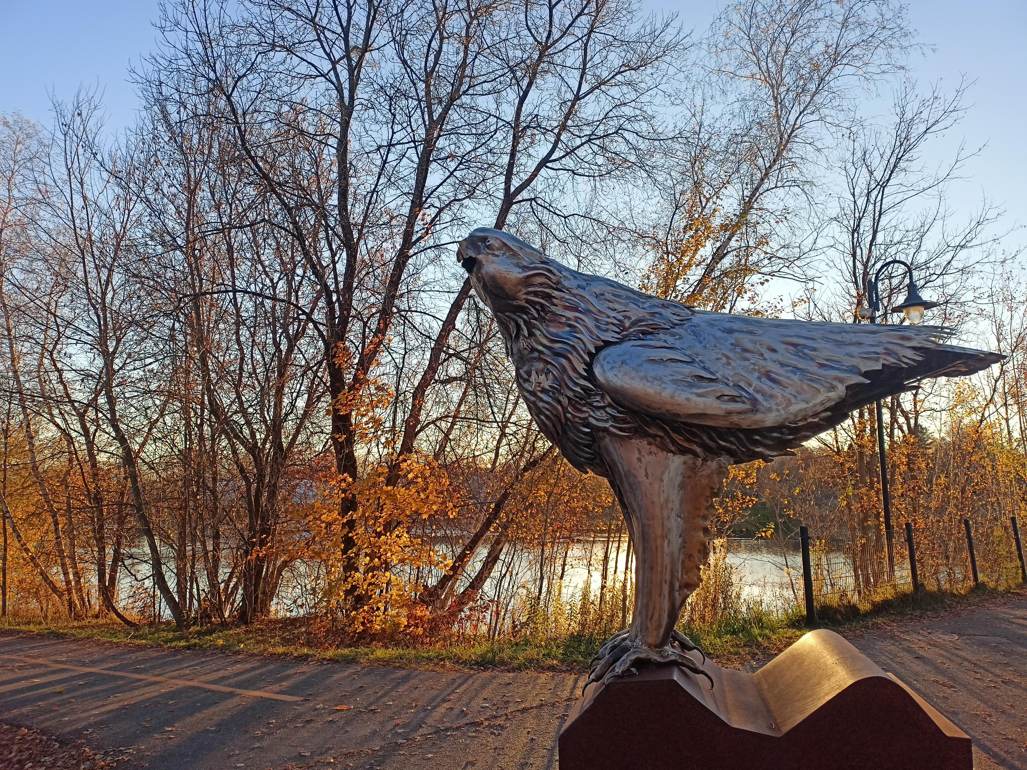 Sculpture d'oiseau devant lac et forêt d'automne, au soleil couchant