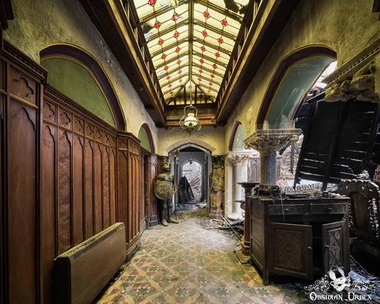 The ruined entrance hall of The Knight's Hotel in Wales, showing a grand skylight, patterned floor tiles, and severe fire damage