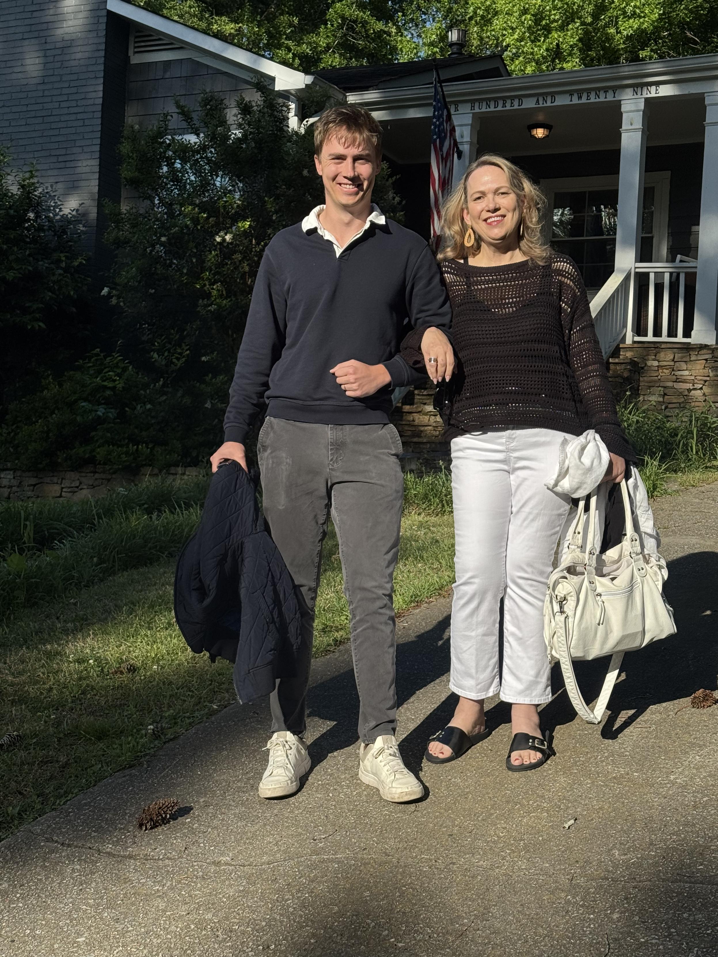 Smiling woman and young man standing on a sidewalk before a house