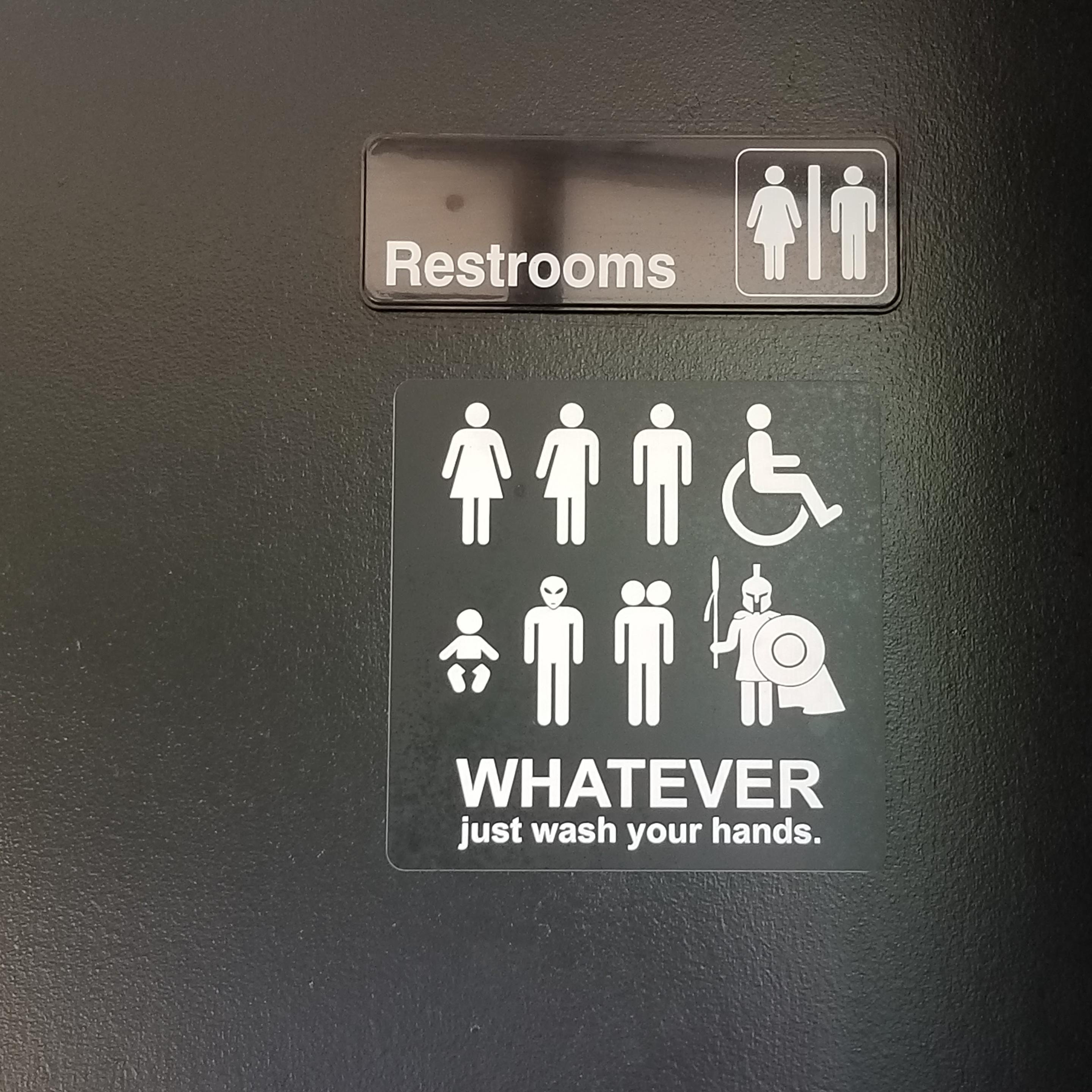 Black and white unisex restroom  sign with male and female figures, plus half man and half woman figure, plus wheelchair figure, plus baby figure, plus grey alien figure, plus 2 headed figure,  plus spartan warrior figure. Followed by the script: WHATEVER just wash your hands.