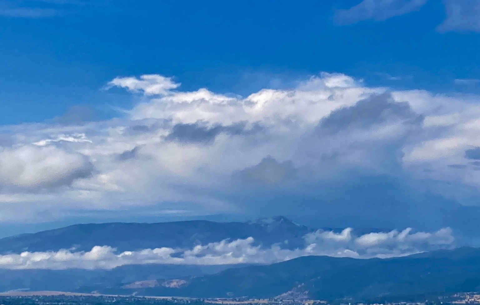 Clouds hide the Bitterroot Mountains, but it’s clear over the valley and above the clouds, creating layers of white and blue.