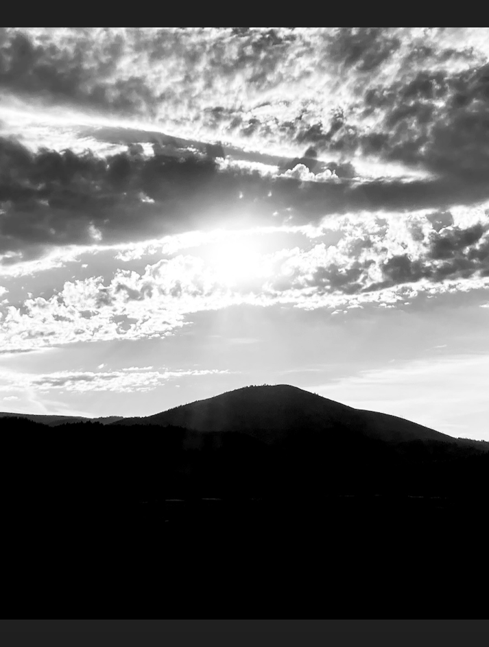 A mountain is silhouetted, the sun above it hidden behind clouds that are also silhouetted, but also forming a criss-cross pattern.