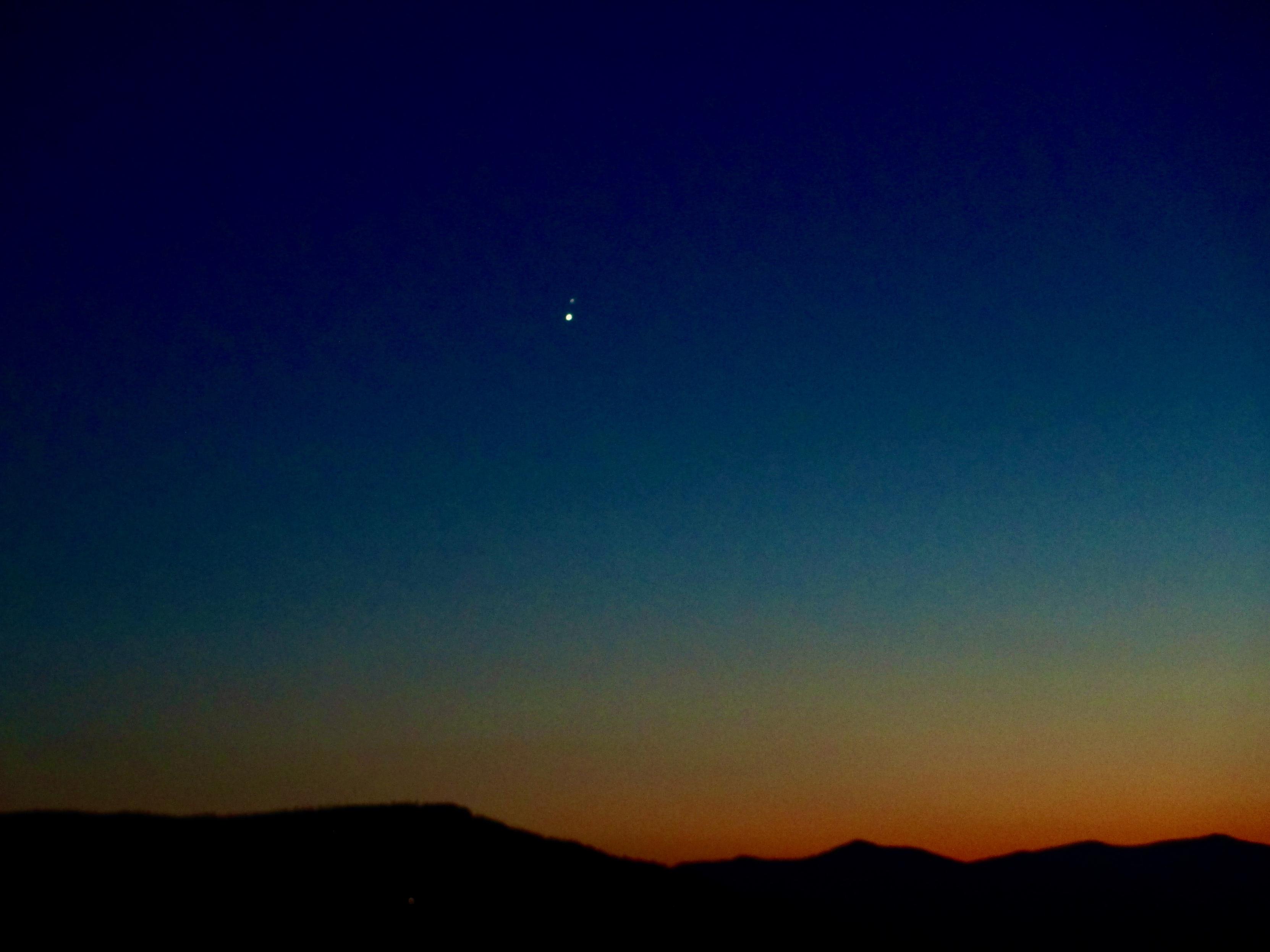 Mountains are silhouetted as a sunset comes to a close. In the darkening sky are two points of light, one Venus and the other Jupiter.