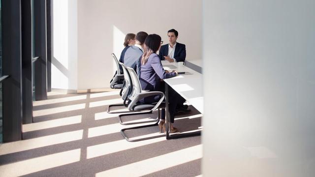 An einem großen Tisch in einem hellen, modernen Büro sitzen Mitarbeiter im Gespräch.