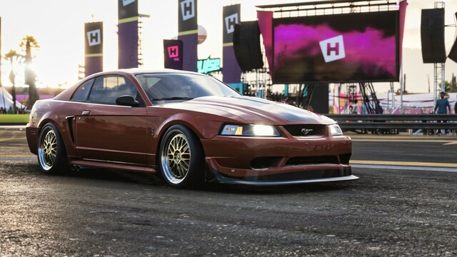 Side shot from the passenger side of an orange and black 2000 Ford SVT Cobra R parked on a drag strip. The wheels are cambered out and sun setting in the background creates an intense contrast, blurring the trees and towers surrounding the strip of asphalt.