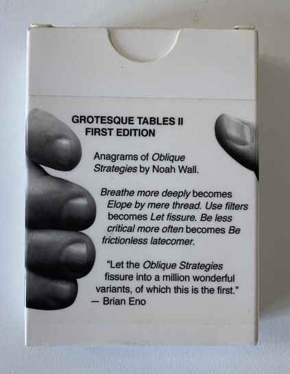 A pack of cards in a box. The box has images of fingers and a thumb on it, as if holding it. There is text on the box, a title: GROTESQUE TABLES II
FIRST EDITION.
And the following: Anagrams of Oblique
Strategies by Noah Wall.
Breathe more deeply becomes
Elope by mere thread. Use filters becomes Let fissure. Be less critical more often becomes Be frictionless latecomer.
"Let the Oblique Strategies fissure into a million wonderful variants, of which this is the first."
- Brian Eno