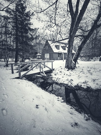 A monochromatic image of the snowy banks of a partial moat of water, in the background the museum center against a barren gardens of Acadia winter sky
