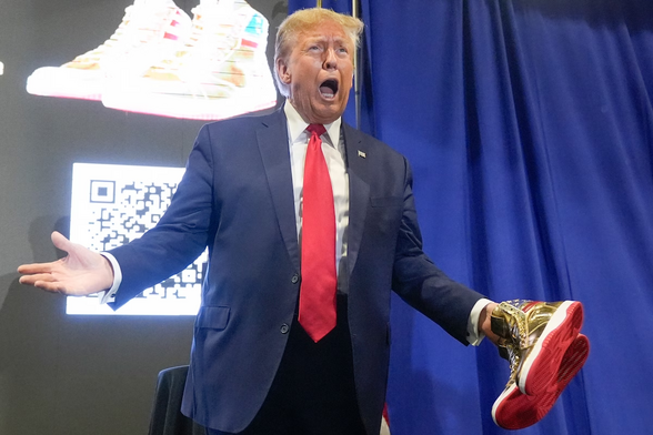 Donald Trump, his mouth open in a wail or shriek of some kind, holding a pair of sneakers that he is hawking to an audience.