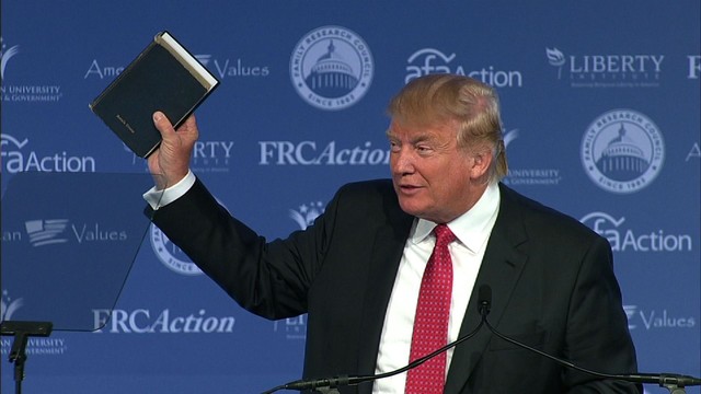 Con artist smirking as he holds up a bible.