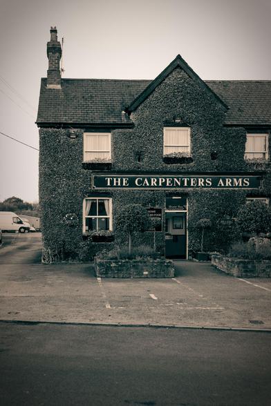 Black and white photo of The Carpenters Arms, a public house with ivy of the frton a gable.