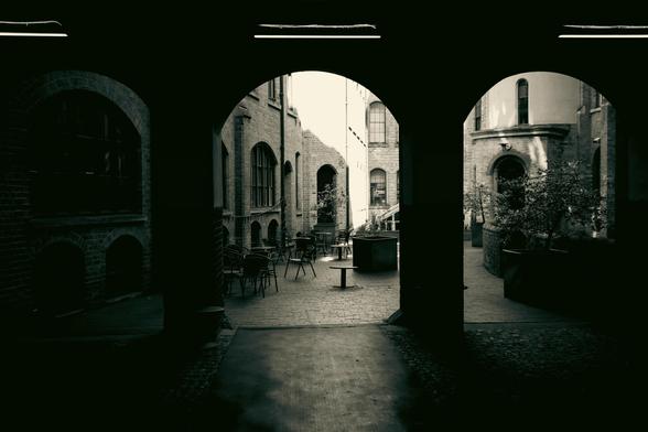 A view of a courtyard with plants, tables and chairs from inside a set of arches.