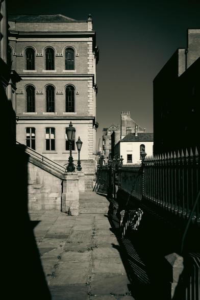 Building in heavy shadows shot from inside the railings looking towards the entrance stairs with old lampposts.