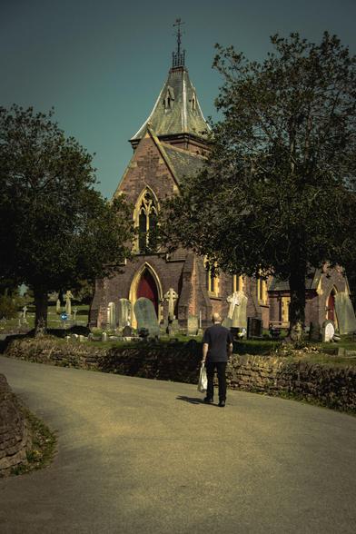 The cemetery chapel in the sunlight; a man walking along the footpath.