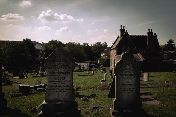 Two gravestones in the foreground; more gravestones and a building behind.