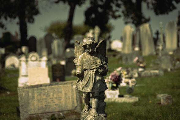 Stone sculpture of an angel against the blurred background of the cemetery.