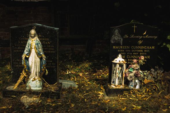 A statue of the Virgin Mary, a lantern, and some dried flowers in front of gravestones.