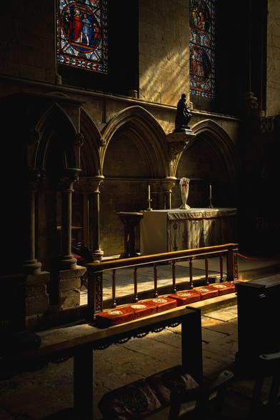 Interior of a gothic cathedral; a side alter captured in the sunlight below a stained-glass window.