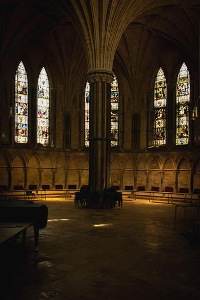 Inside a gothic cathedral is a round chamber, the Chapter House, with stained-glass windows and an ornate column in the middle.