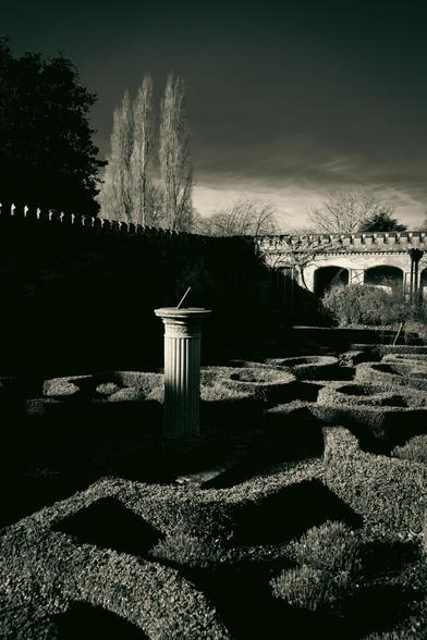 Walled garden at a stately manor; a sun dial in the centre of short, patterned hedges.