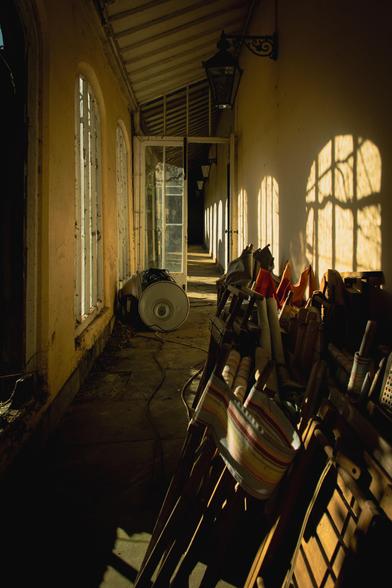Corridor with sunlight flooding through the windows; chairs and other items stacked up against the wall.