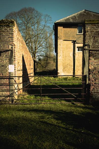 A metal gate, exterior of the walled garden, and outbuildings of the manor house.