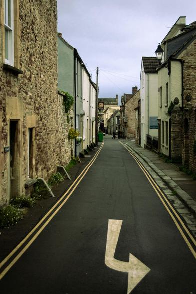 Narrow, rustic street with old houses, double yellow lines (no parking!) and a white, painted arrow (turn left; view is upside down).