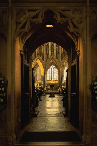 View through a passage into the choir, with arches and stained-glass window in the back.