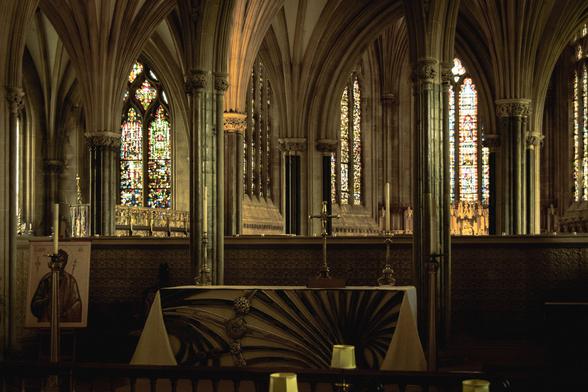 An alter with candles and a crucifix; the pillars and stained-glass windows of the apse are behind.