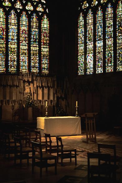 An alter with two candles, stone carvings and stained-glass windows in a chapel in the Cathedral.