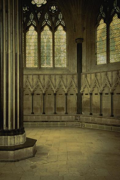 Inside the Chapter House: an ornate pillar, stalls carved out of stone, and arched windows.