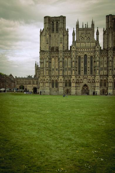 West front elevation of Wells Cathedral from across the green under a cloud sky; the right of the front is deliberately cropped in a dramatic way.