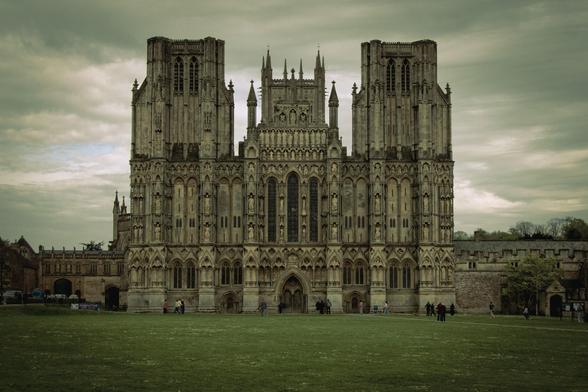 West front elevation of Wells Cathedral viewed from across the Green under a cloudy sky.