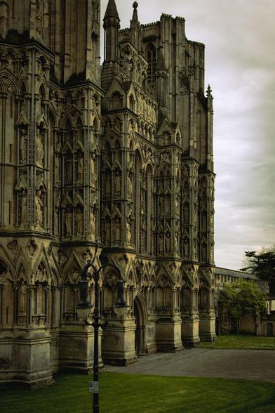 The west front of Wells Cathedral under a cloudy sky, looked at from an angle from the south corner.