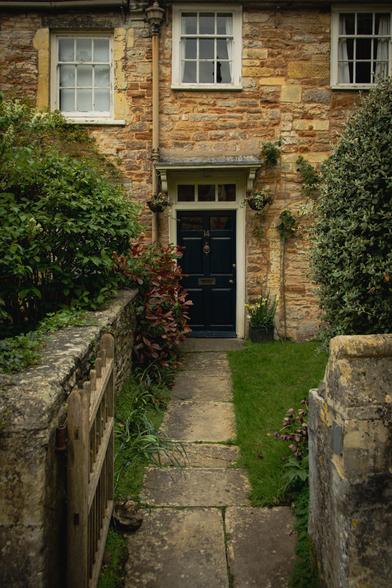 Garden path leading to a blue front door in an old house; shrubs and windows.