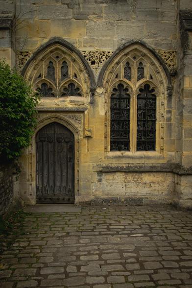 Gothic architecture: a cobbled street, arched windows, and an old wooden door in a stone building.