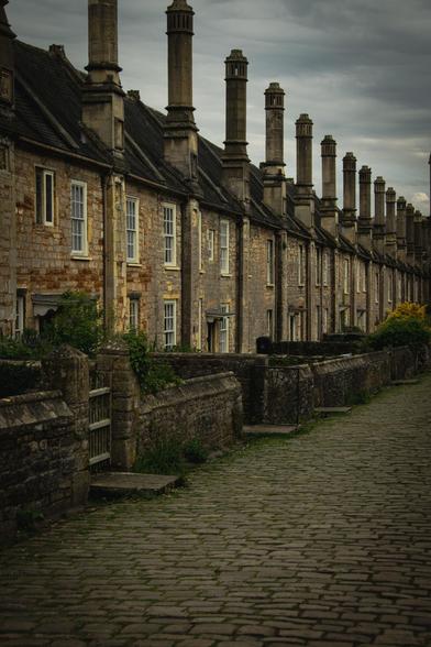 A row of old stone houses with high chimney stacks on a cobbled street. Receding lines.