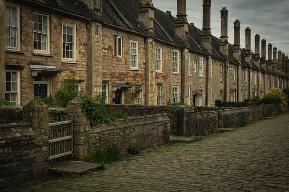 A row of old stone houses with high chimney stacks on a cobbled street. Receding lines.