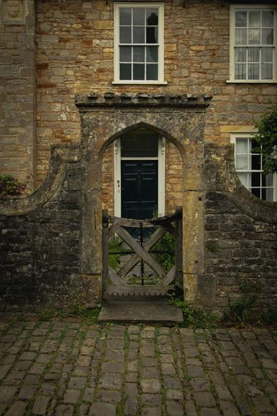 An old brick house on a cobbled street. An arched stone entry with wooden gate leads to the front door.