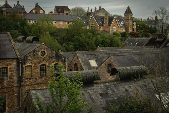 View over the rooftops of an old industrial building towards house (one Victorian with a turret) higher up on the hill.