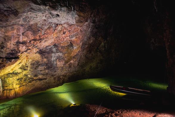 View inside the cave. Spotlights light up the rock formations and an underground river.  A rowing boat is moored on the right.