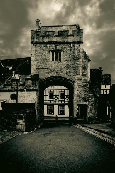 Monochrome image of a short road leading to a historic stone tower and gatehouse.
