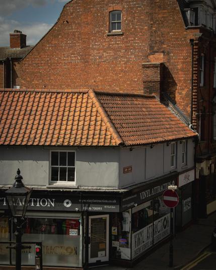 View from higher up of a streetcorner in an English town: a red brick building above a red-tiled roof above a white-and-black fronted shop.