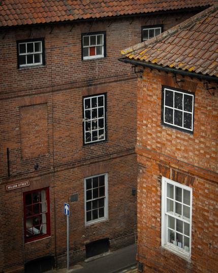 A streetcorner with two red-brick houses with with-framed windows and red-tiled roofs. A traffic sign is below the streetsign which reads 'Wilson Street'.
